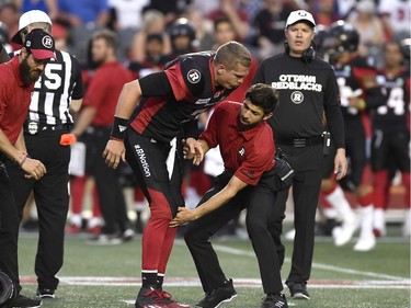 A trainer holds the leg of Ottawa Redblacks quarterback Trevor Harris (7) after a collision, as head coach Rick Campbell heads onto the field, during pre-season CFL action against the Montreal Alouettes in Ottawa on Thursday, May 31, 2018.