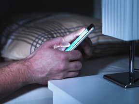In this stock photo, a man texts on a phone in a dark bedroom.