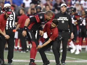 A trainer holds the leg of Ottawa Redblacks quarterback Trevor Harris (7) after a collision, as head coach Rick Campbell heads onto the field, during pre-season CFL action against the Montreal Alouettes in Ottawa on Thursday, May 31, 2018. (THE CANADIAN PRESS/PHOTO)