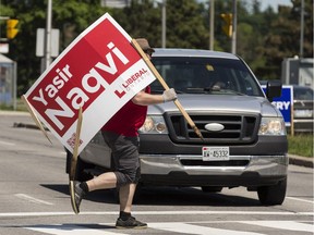 A worker runs across Carling Avenue with a Yasir Naqvi campaign sign that he removed from property on Island Park Drive in the Ottawa-Centre riding where the Liberal candidate was defeated in the provincial election. June 8, 2018.
