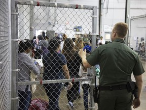 In this photo provided by U.S. Customs and Border Protection, a U.S. Border Patrol agent watches as people who've been taken into custody related to cases of illegal entry into the United States, stand in line at a facility in McAllen, Texas, Sunday, June 17, 2018.