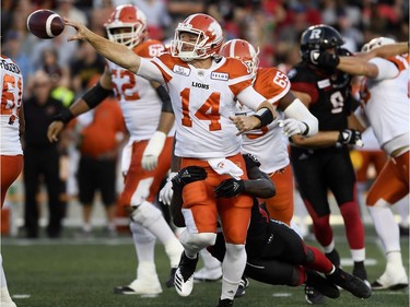 Lions quarterback Travis Lulay (14) flips the ball away to avoid a sack by Redblacks defensive end A.C. Leonard (99).