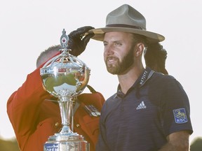 Dustin Johnson of the United States hoists the Canadian Open championship trophy and a Royal Canadian Mounted Police officer places his Stetson on his head at the Glen Abbey Golf Club in Oakville Ont., on Sunday, July 29, 2018.