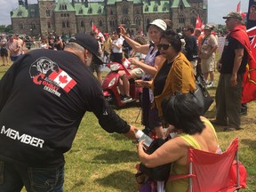 A member of the "Canadian Combat Coalition" protesting on Parliament Hill hands a water bottle to a child on Saturday.