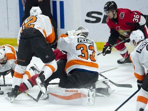 Philadelphia Flyers goaltender Calvin Pickard pulls off his mask as Senators winger Ryan Dzingel and Flyers' Michael Raffl slide into him during Wednesday's game. (THE CANADIAN PRESS)