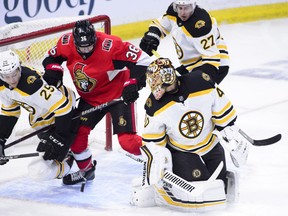 Boston Bruins goaltender Tuukka Rask looks back as the puck bounces around in front of teammate Brandon Carlo and Senators centre Colin White in Ottawa on Tuesday night. (Sean Kilpatrick/The Canadian Press)