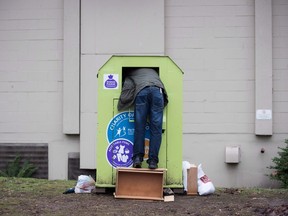 A man tries to retrieve items from a clothing donation bin in Vancouver last month. The District of West Vancouver is shutting clothing donation bins and looking at options to either make them more secure or remove them following the death of a man on Dec. 30.