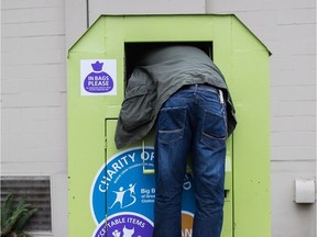 A man tries to retrieve items from a clothing donation bin in Vancouver last month. The District of West Vancouver is shutting clothing donation bins and looking at options to either make them more secure or remove them following the death of a man on Dec. 30.