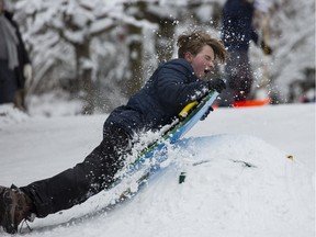 A boy rides off of a jump sideways while sledding on a hill.