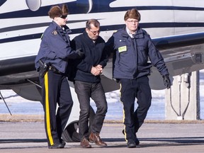 RCMP officers escort a suspect arrested in a money laundering network off an airplane in St-Hubert, Que. on Monday, February 11, 2019.