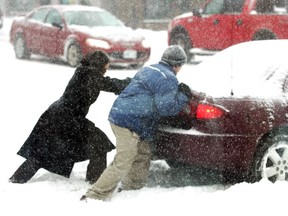 Two people push a car stuck in the snow and ice.