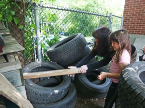 Lianna Levesque and her daughter Maddisin-Lynn try to poke the rats out of tires near their rental home in Overbrook on Tuesday.