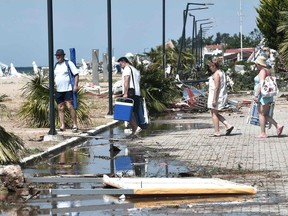 Tourists pass next to a damaged road after a storm, at a beach bar in Nea Plagia, in Chalkidiki, Northern Greece, on Friday.
