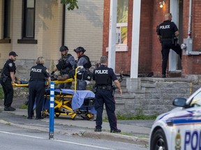 Members of the Ottawa Police Service Tactical Unit and tactical paramedics with other officers assist in transporting an unidentified man to a waiting ambulance at a crime scene on Lyon Street on Friday evening.