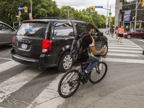 A cyclist holding a cellphone rides on the sidewalk at Yonge and King Sts. (Ernest Doroszuk, Toronto Sun)