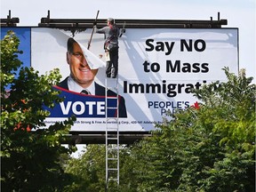 A worker removes a billboard featuring the portrait of People's Party of Canada Leader Maxime Bernier and its message, "Say NO to Mass Immigration" in Toronto on Aug. 26, 2019.
