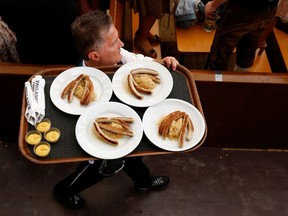 A waiter carries plates with sausages.