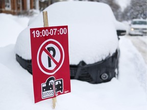 A car covered in snow parked alongside a snow removal sign.