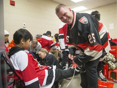 Former Senator Chris Neil helps Samuel Sum, 11, and other kids get ready in the dressing rooms as Ottawa Senators owner Eugene Melnyk hosted over 100 children at the 16th annual Eugene Melnyk Skate for Kids at Canadian Tire Centre on Friday, Dec. 20.