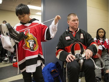 Samuel Sum, 11, puts laces in his skates as former Senator Chris Neil helps kids get ready in the dressing rooms as Ottawa Senators owner Eugene Melnyk hosted over 100 children at the 16th annual Eugene Melnyk Skate for Kids at Canadian Tire Centre on Friday, Dec. 20.