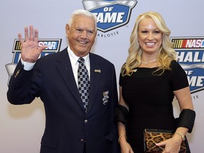 NASCAR Hall of Fame driver Junior Johnson waves to the media as he stands with his wife, Lisa, on the red carpet before the NASCAR Hall of Fame induction, Wednesday, Jan. 29, 2014, in Charlotte, N.C. (AP Photo/Bob Leverone)