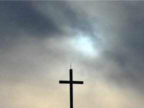 The sun is obscured by clouds behind a steeple and cross.