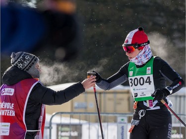 Coralie Beauchamp grabs a drink from a volunteer during the 27 km Classic event at the Gatineau Loppet. February 15, 2020. Errol McGihon/Postmedia