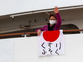 A woman waves after hanging a Japanese flag that reads "shortage of medicine" on the cruise ship Diamond Princess.