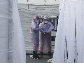 Medical staff wearing protective suits check documents as they wait for people with suspected symptoms of the new coronavirus, at a testing facility in Seoul, South Korea, Wednesday, March 4, 2020.