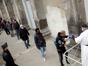 Priest Francesco wearing a face mask and protective gloves, hands out bags of food to homeless and poor people, as the spread of coronavirus disease (COVID-19) continues, in Naples, Italy, March 27, 2020.