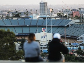 People sit on a hill overlooking Dodger Stadium on what was supposed to be Major League Baseball's opening day, now postponed due to the coronavirus, on March 26, 2020