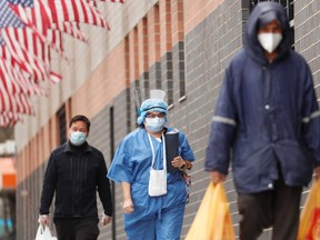 A healthcare worker walks between delivery people while wearing personal protective equipment outside of Elmhurst Hospital during the ongoing outbreak of the coronavirus disease (COVID-19) in the Queens borough of New York, U.S., April 20, 2020.
