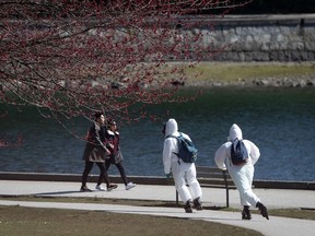 Two people wearing personal protective equipment, including respirators and coverall suits in-line skate on the seawall at Stanley Park in Vancouver on Sunday, April 5, 2020.