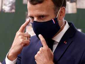 France's President Emmanuel Macron wears a protective face mask with a blue-white-red coloured ribbon as he gestures while speaking with schoolchildren during a class during a visit to the Pierre de Ronsard elementary school in Poissy, France, May 5, 2020, as France readies to face an ease in the coronavirus lockdown measures.