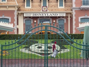 In this file photo an employee cleans the grounds behind the closed gates of Disneyland Park on the first day of the closure of Disneyland and Disney California Adventure theme parks as fear of the spread of coronavirus continue, in Anaheim, Calif., on March 14, 2020.