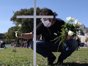 A man places flowers near a cross during a symbolic protest and tribute for health workers who died from COVID-19, in Sao Paulo, Brazil, Saturday, June 20, 2020.