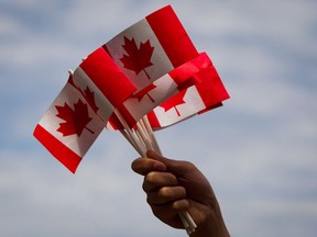 A volunteer waves Canadian flags while handing them out to people during Canada Day festivities in Vancouver, B.C., on Monday, July 1, 2013. COVID-19 means the true north is not entirely free this Canada Day, but a new survey suggests that's not going to change how many people mark the holiday.