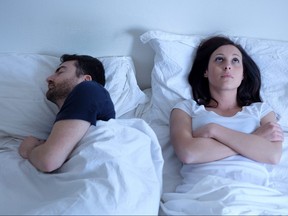 Sad and thoughtful woman awake while husband is sleeping in bed