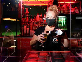 Bartender Tasha Holt pours a beer while wearing her mask at the Orange Monkey bar and billiards in Ottawa.