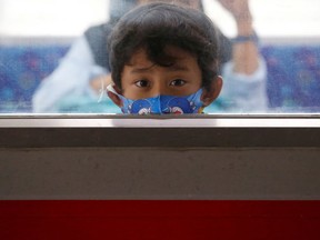 A child wearing a protective mask looks through a window.