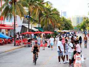 A woman rides her bike past pedestrians on Ocean Drive in the South Beach neighbourhood of Miami Beach, Fla., Friday, July 3, 2020.