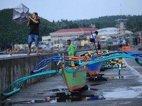 A resident holds onto his umbrella in strong wind as others stand by their wooden boats along the coastal area of Legaspi City, Albay province south of Manila on october 25, 2020, ahead of tropical storm Molave's expected landfall.