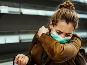 A woman in a mask sneezes into her arm