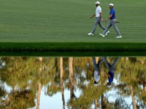 Dustin Johnson and Jon Rahm, right, walk around the pond in front of the 16th green at Augusta National Golf Club during the third round of the Masters on Saturday.