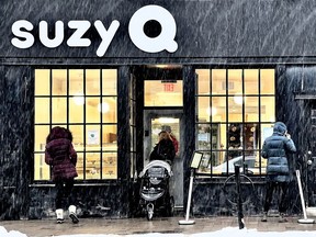 People try to seek shelter from a snow squall as they line up outside a suzy Q doughnut shop in Ottawa on Wednesday.