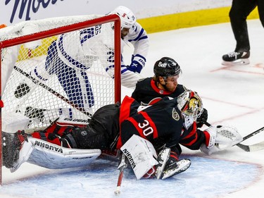 Senators goaltender Matt Murray reaches around teammate Josh Norris to grab the puck before Maple Leafs winger Wayne Simmonds can get there with his stick.