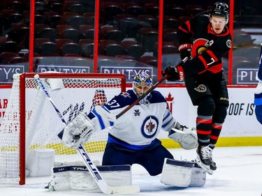 Senators left-winger Brady Tkachuk tips a shot on Jets goaltender Connor Hellebuyck during first-period action.