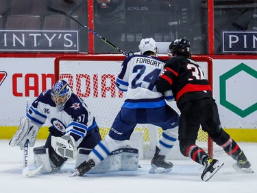 Jets goaltender Connor Hellebuyck makes a save as Senators centre Colin White is checked by defenceman Derek Forbort during second-period action.
