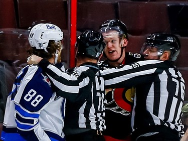 Senators left-winger Brady Tkachuk and Jets defenceman Nathan Beaulieu exchange words during a late third-period scrum despite being physically separated by on-ice officials Derek Nansen and Michel Cormier.