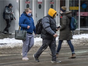 Pedestrians wearing masks walk across Yonge Street at Dundas Street in Toronto on Tuesday, Feb. 16, 2021.